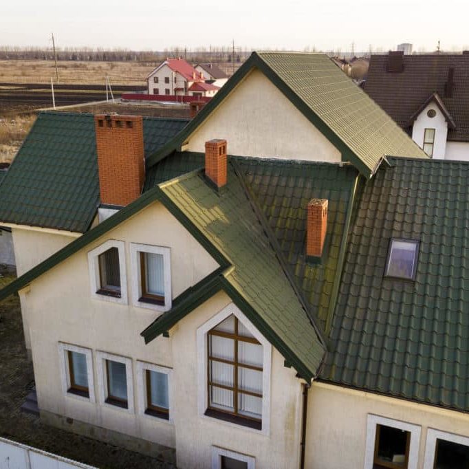 Aerial view of new residential house cottage and garage or barn with shingle roof on fenced yard on sunny day.