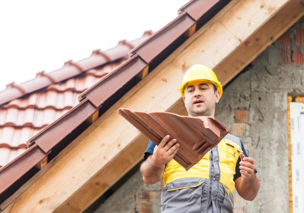 The builder stands on the background of a new building, holding a piece of tile in his hand